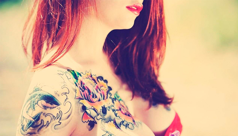 Улыбающаяся женщина с цветочной татуировкой на плече.