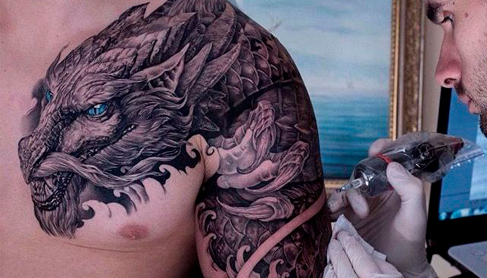 Мужчина с драконом на спине получает тату на руке от тату-мастера.