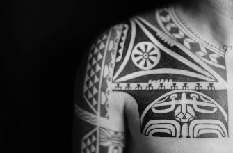 Красочная татуировка в стиле хайда на руке человека, изображающая тотемное животное с орнаментами.