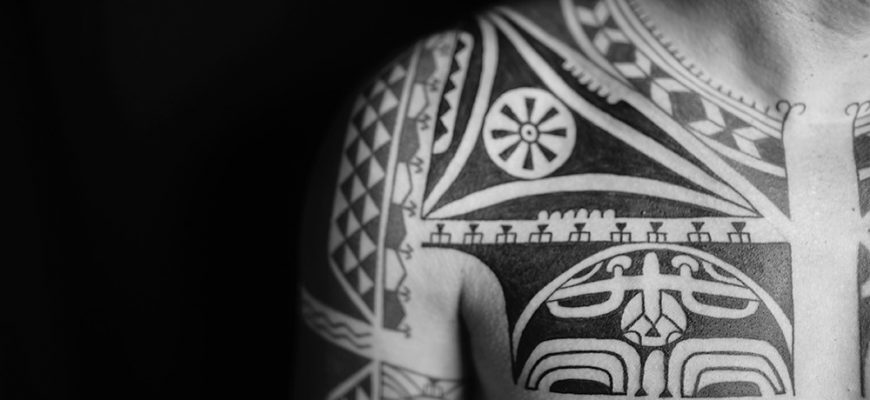 Красочная татуировка в стиле хайда на руке человека, изображающая тотемное животное с орнаментами.